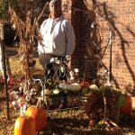 Picture of Danyel Armstrong behind fall decorations of pumpkins, cornstalks, and cotton which he designed.