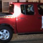 Red four-door truck trimmed in Christmas decorations with poster with Christmas parade theme on front passenger door.